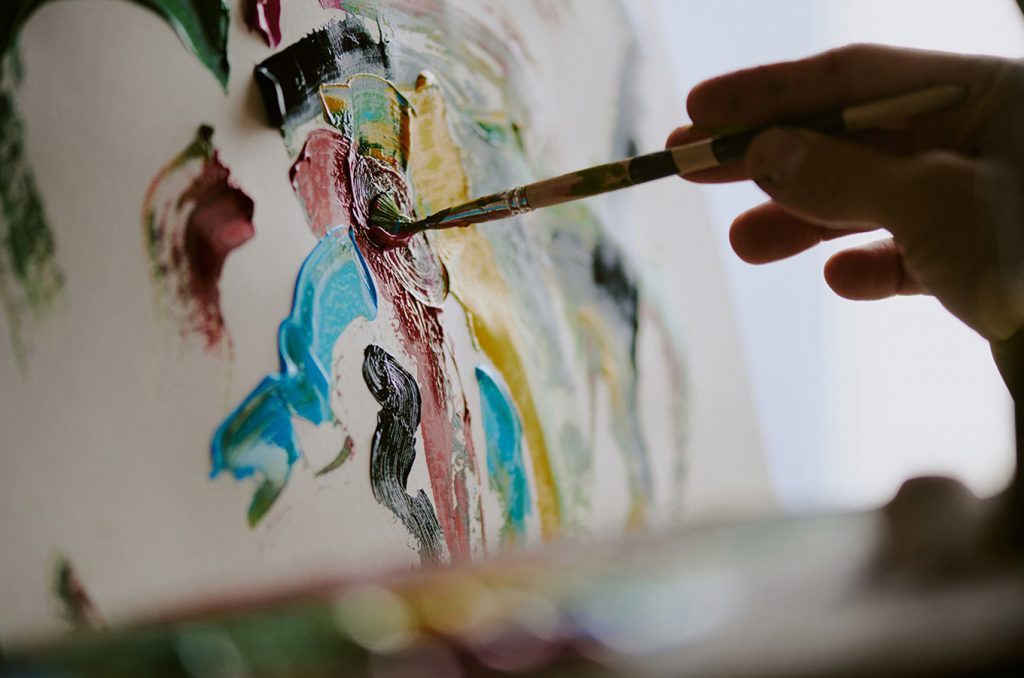 a hand holding a paint brush painting an abstract on canvas